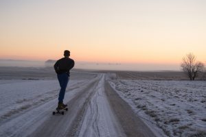 Mensch auf Skateboard fährt überfrorenen Feldweg im Sonnenaufgang entlang